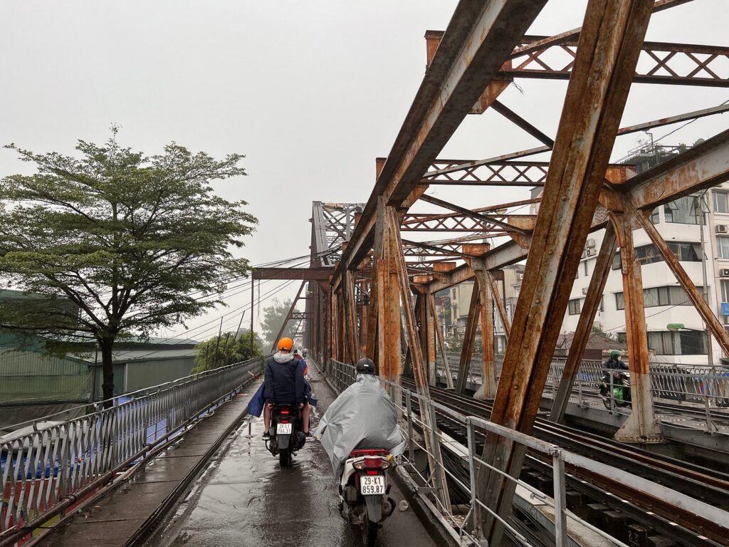 Motorbikes crossing Long Bien Bridge beside its railway tracks on a rainy day.
