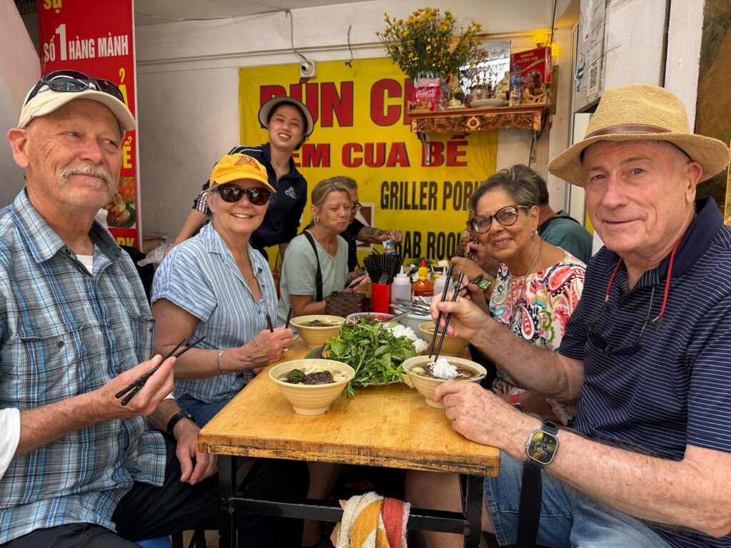 Diners sharing a meal around a wooden table at a Hanoi food stall.