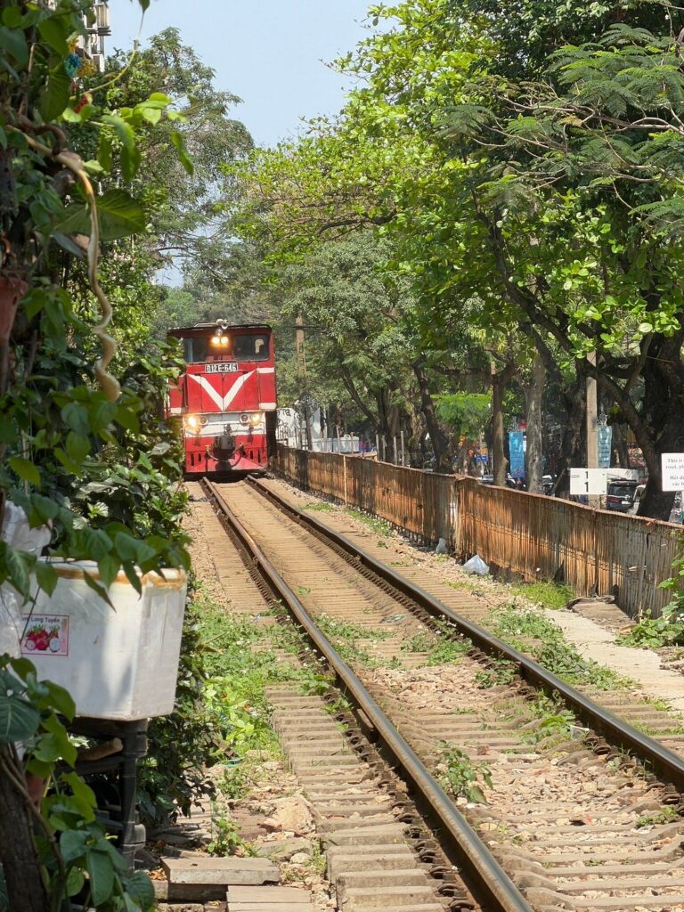 A red locomotive on railway tracks lined with trees in Hanoi.